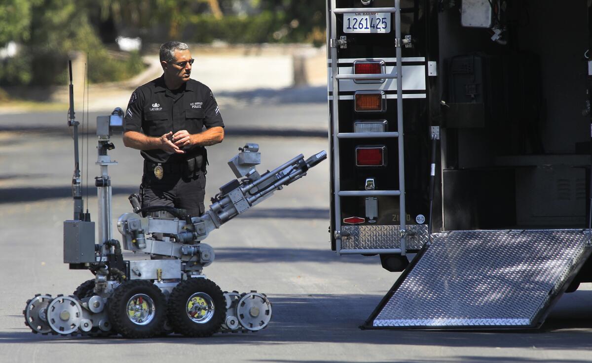 An LAPD bomb squad officer walks along the 16500 block of Simonds Street with a bomb squad robot after securing a Granada Hills home where possible explosives and firearms were found.
