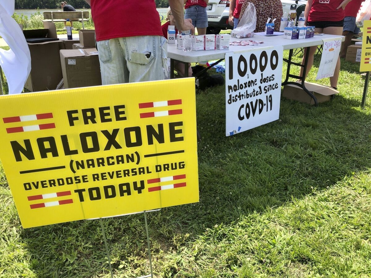 FILE - Signs are displayed at a tent during a health event on June 26, 2021, in Charleston, W.Va. Volunteers at the tent passed free doses of naloxone, a drug that reverses the effects of an opioid overdose by helping the person breathe again. The U.S. needs a more nimble strategy and Cabinet-level leadership to counter its festering opioid epidemic, a bipartisan congressional commission said Tuesday. (AP Photo/John Raby, File)