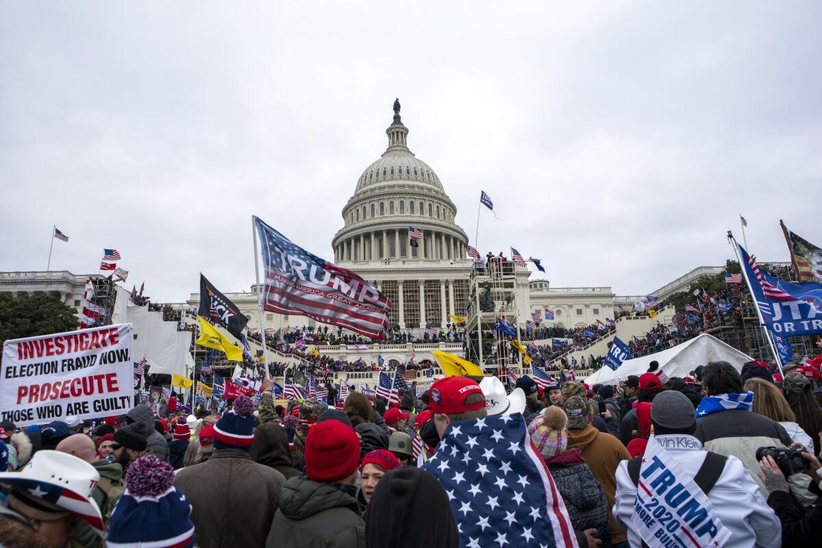 A crowd waves Trump flags in the foreground as people attack the U.S. Capitol on Jan. 6, 2021. 