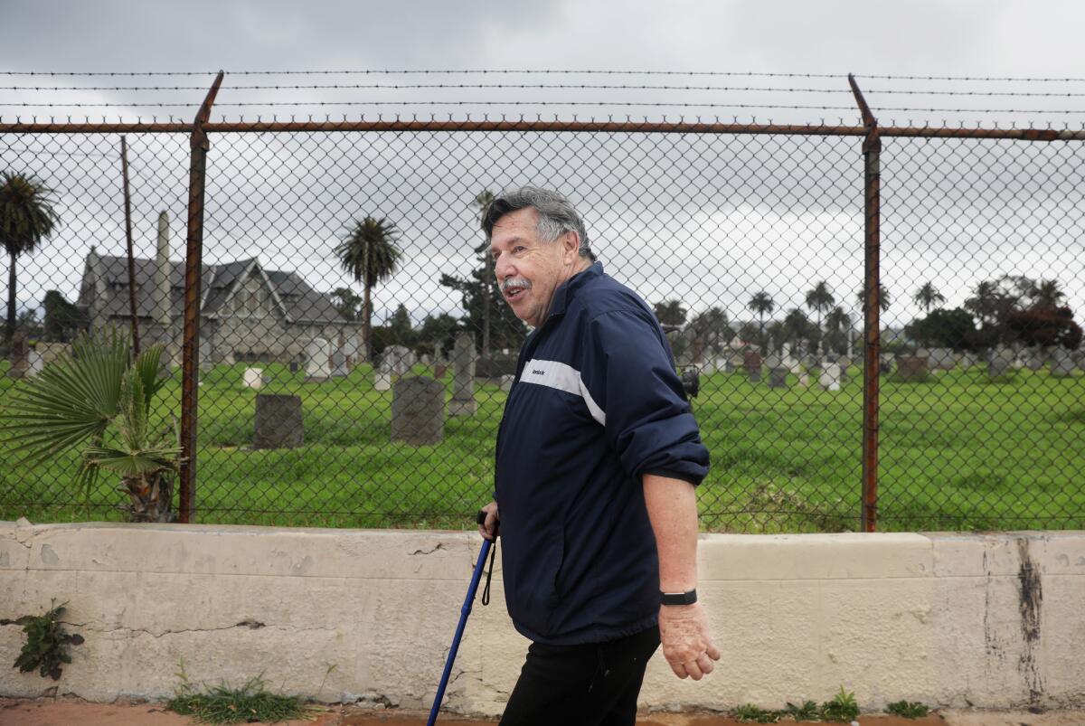 A smiling man with a cane walking past a cemetery