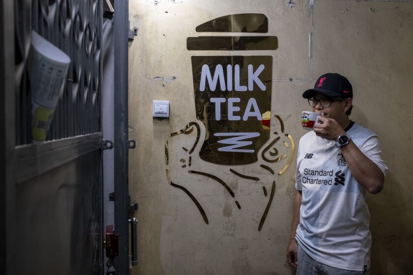 Eric Tam, un gerente de seguros que se mudó a Liverpool con su familia en junio, posa para una foto tras una entrevista el 3 de noviembre de 2022, en Hong Kong. El letrero dice: "Té con leche". (AP Foto/Vernon Yuen)