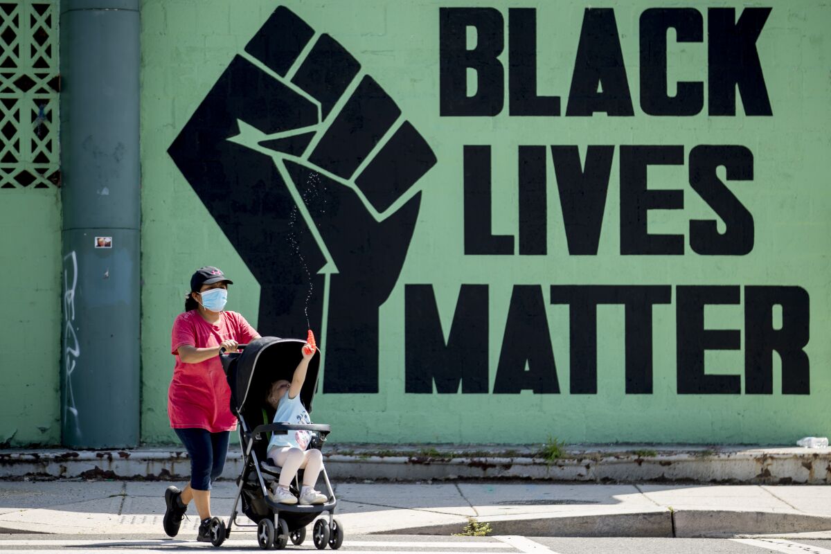 FILE - A girl in a stroller plays with a squirt gun as a woman pushes her past a Black Lives Matter mural in the Shaw neighborhood in Washington, Monday, July 13, 2020. The National Urban League released its annual report on the State of Black America on Tuesday, April 12, 2022, and its findings are grim. This year’s Equality Index shows Black people still get only 73.9 percent of the American pie white people enjoy. (AP Photo/Andrew Harnik, File)