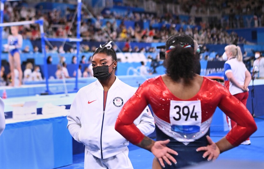 Simone Biles stands with her hands in the pockets of her warmup jacket, looking into the distance.