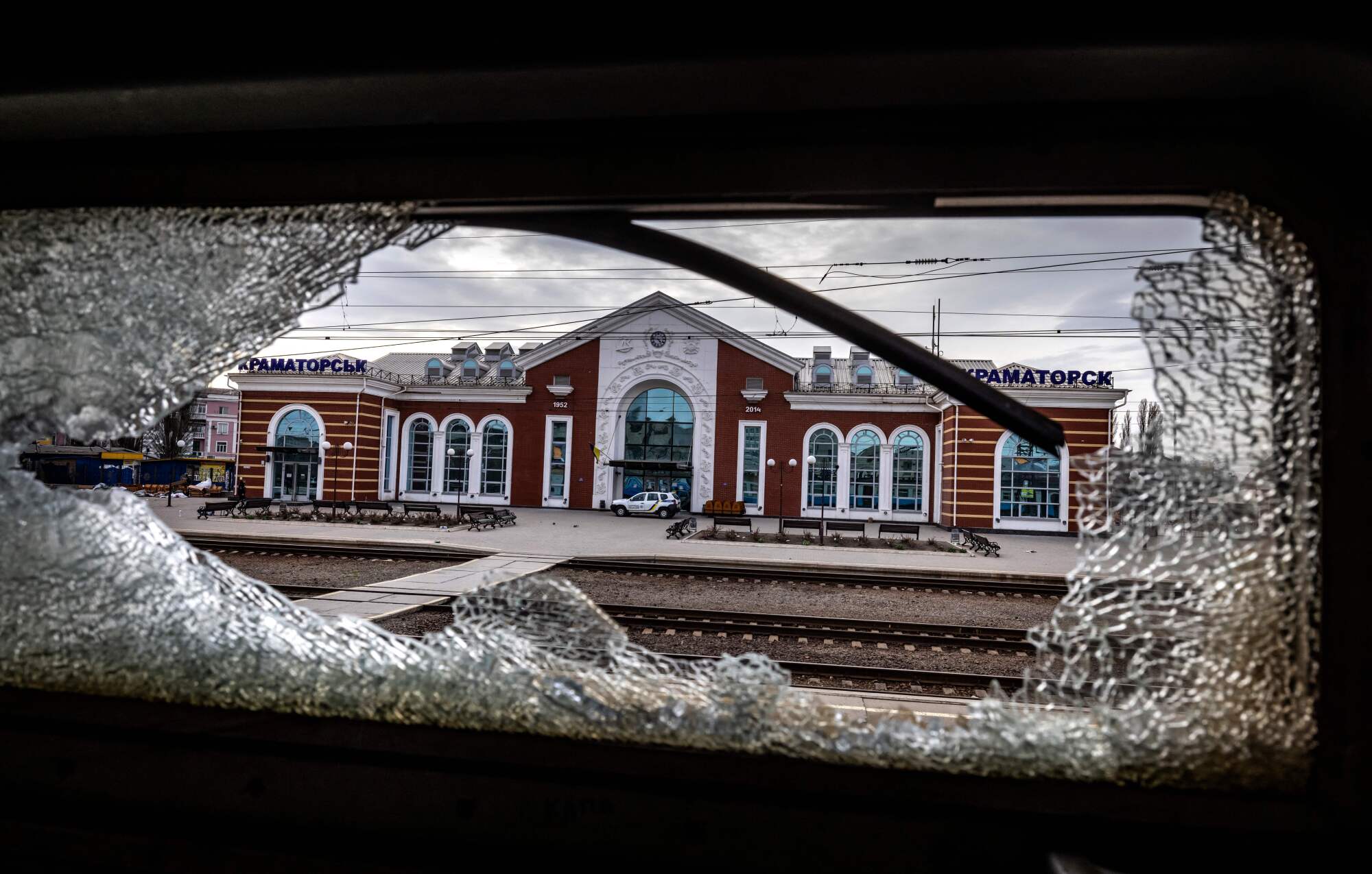 A train station is framed through the shattered glass of a train window.