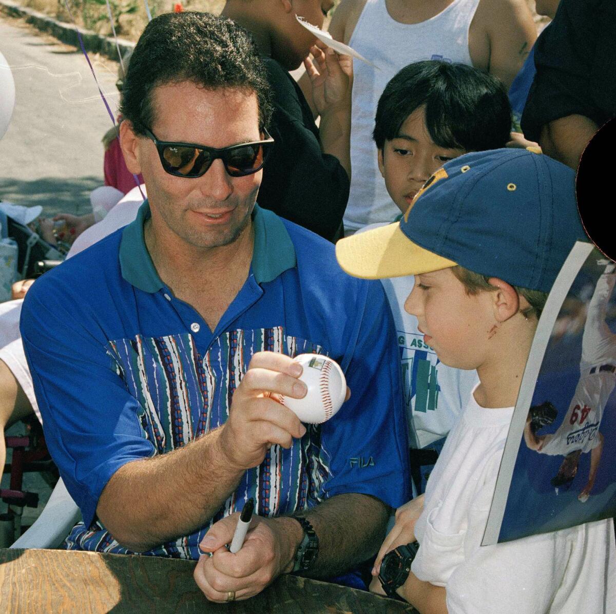 Dodgers pitcher Tom Candiotti shows a young fan a "knuckle hold" during an event.