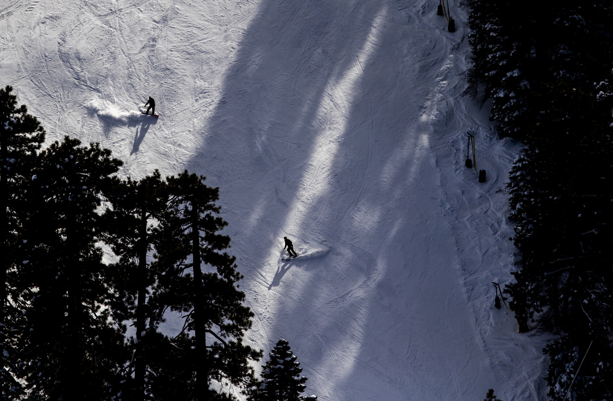 A skier and snowboarder make turns amidst the shadows while sliding down the mountain thanks to snow from recent storms
