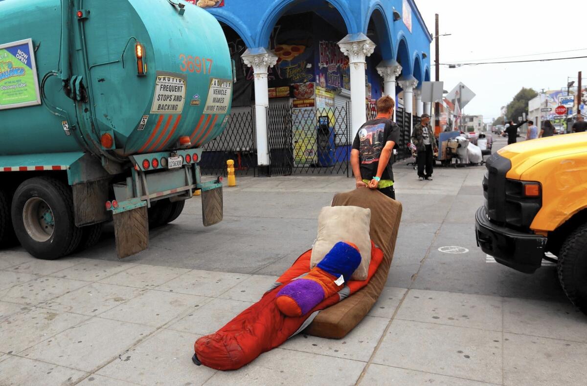 Marcus Steinlechner, 22, drags his bedding between a garbage truck and a city sanitation truck during a sweep of homeless encampments on the boardwalk at Venice Beach on June 26.