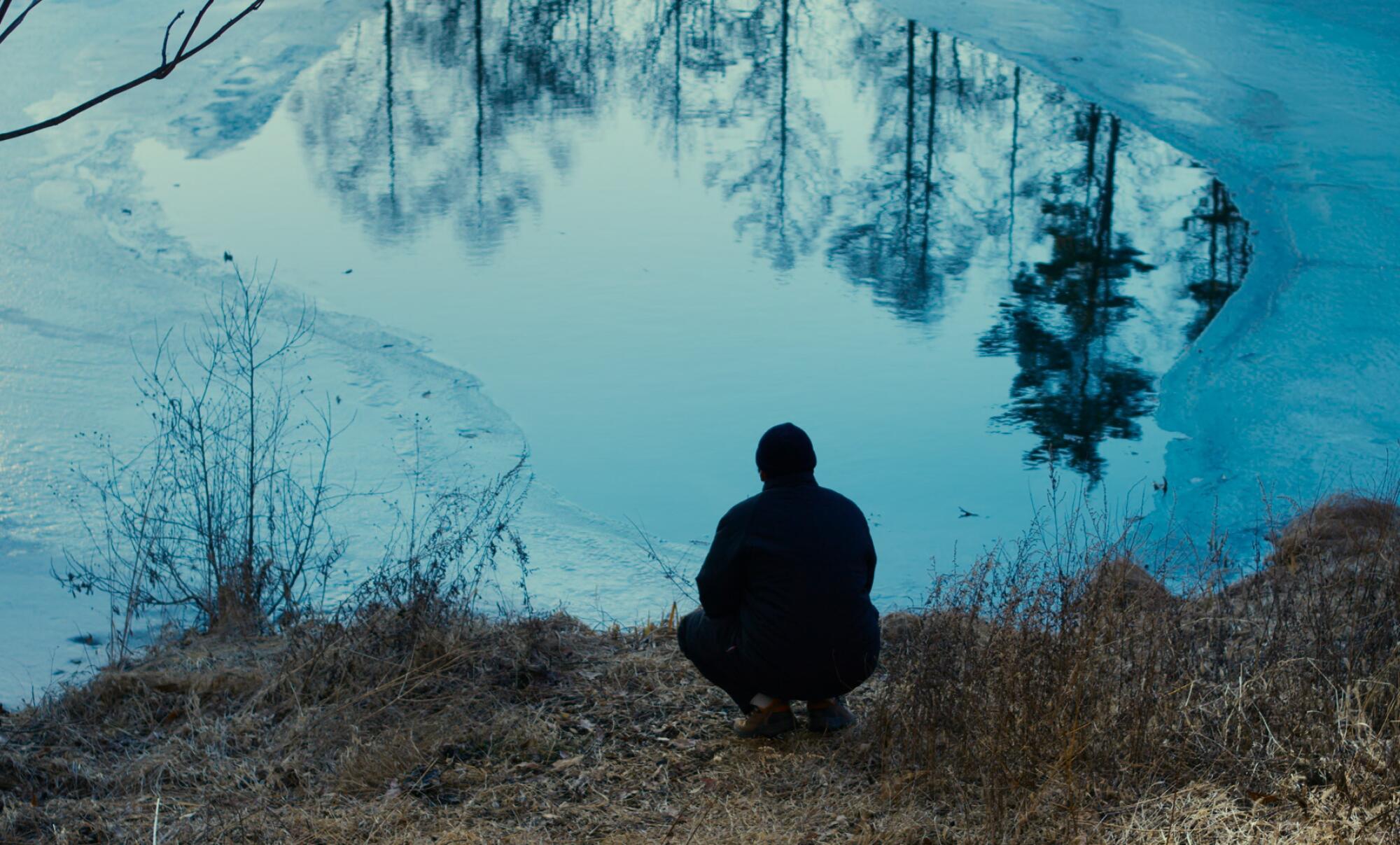 A man sits by a pond.