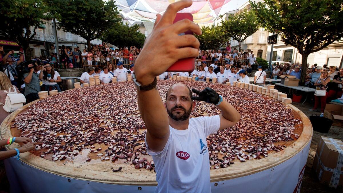 Mandatory Credit: Photo by Brais Lorenzo/EPA-EFE/REX/Shutterstock (9782669a) A man takes a selfie next to a big octopus 'tapa' (a Spanish typical small tasting plate) cooked in the Galician way in O Carballino, Galicia, north-eastern Spain, 07 August 2018, where locals are trying to beat a record set by them last year by cutting 400 kilograms of octopus and serving it as a huge tapa. People gather to beat new record of octupus tapa, O Carballi? (Ourense), Spain - 07 Aug 2018 ** Usable by LA, CT and MoD ONLY **