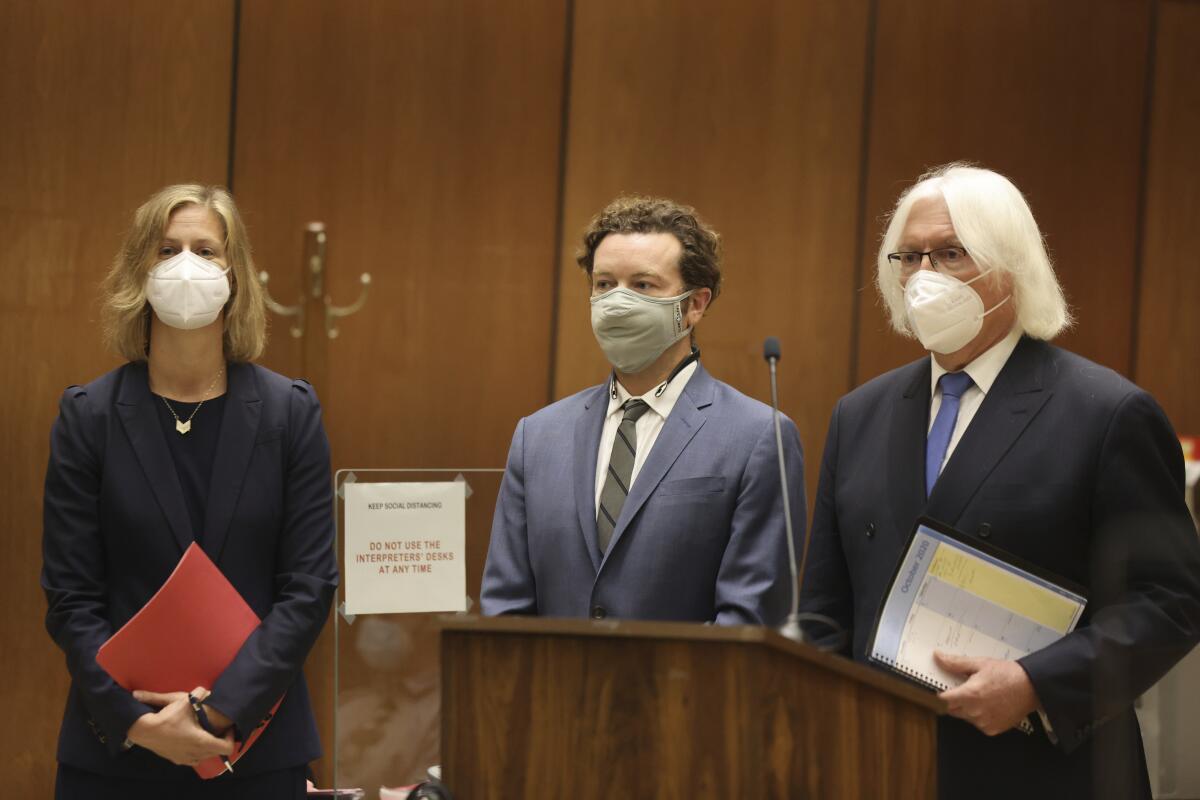 Three masked people standing near a lectern in a courtroom