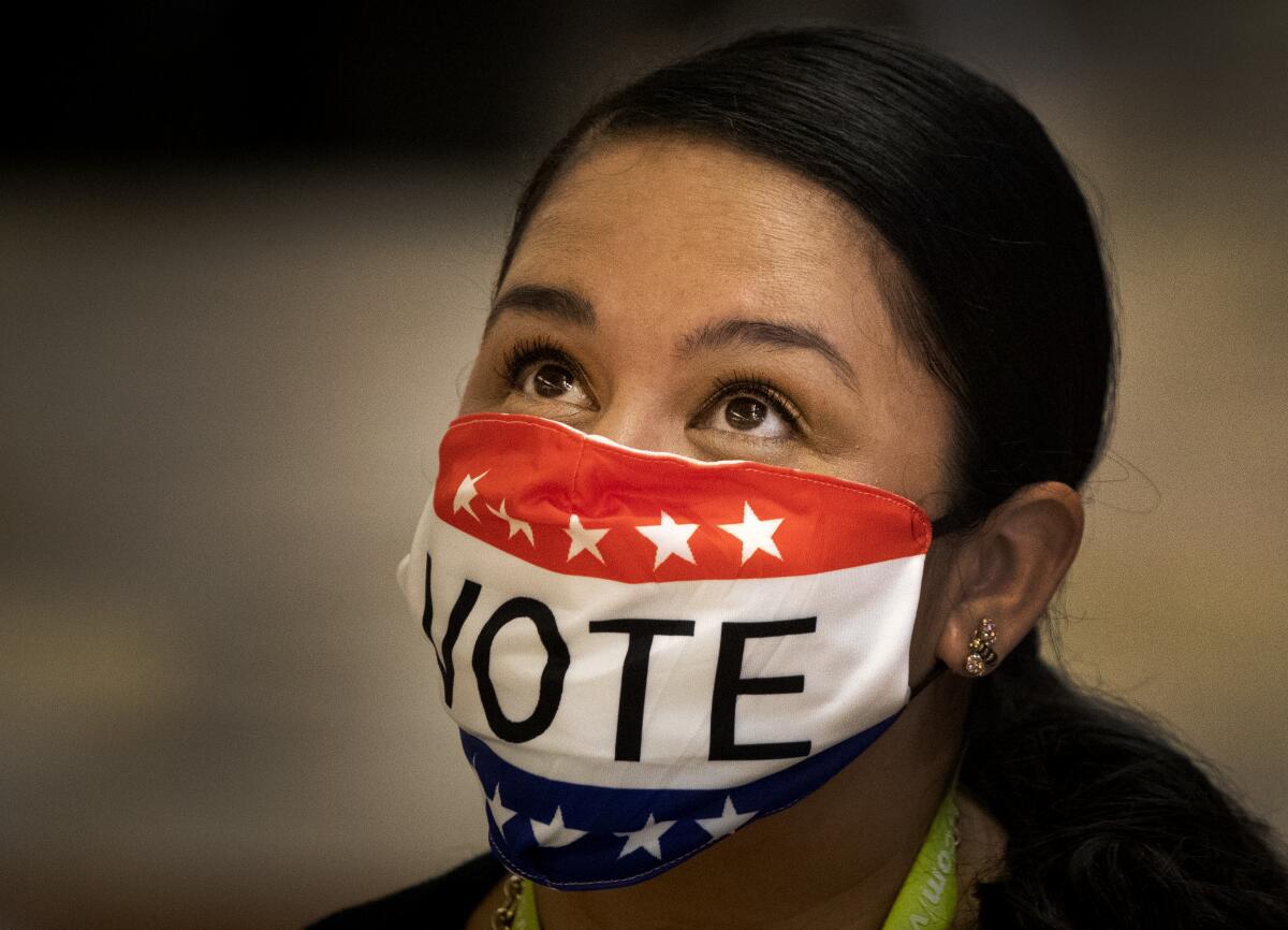 Election worker Melissa Balderas wears a topical mask while assisting early voters Monday at the Honda Center in Anaheim.