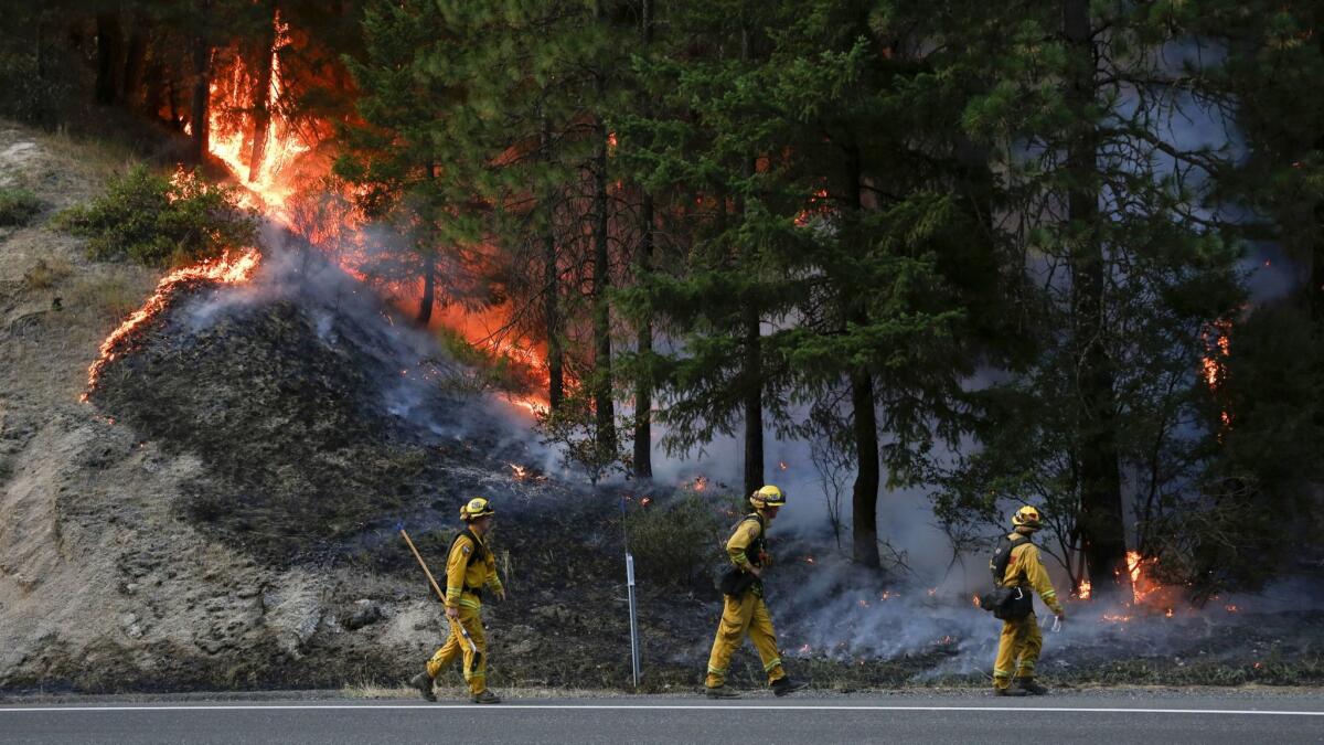 Firefighters monitor flames above California 299 while battling the Carr fire west of Redding on Monday.