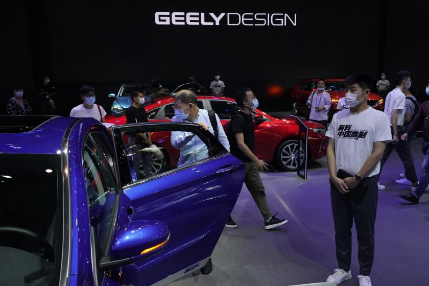 FILE - Visitors look at cars produced by Geely at the Auto China 2020 show in Beijing on Sept. 27, 2020. Geely Holding Group, one of China's biggest independent automakers, has bought a 7.6% stake in British luxury brand Aston Martin Lagonda and said Friday, Sept. 30, 2022, that it looks forward to potential opportunities to collaborate. (AP Photo/Ng Han Guan, File)