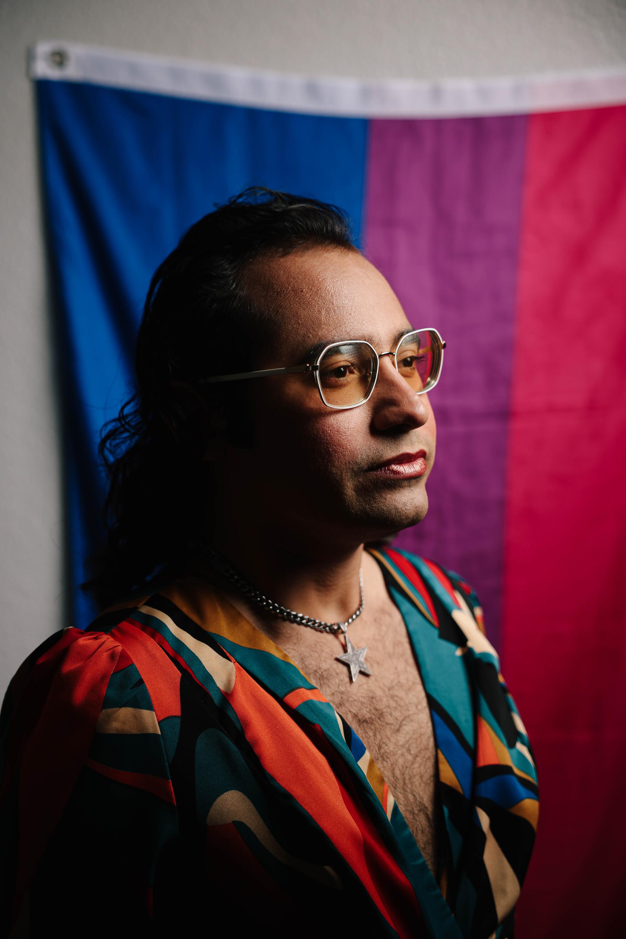 Raul Urena poses for a portrait in front of a rainbow flag.