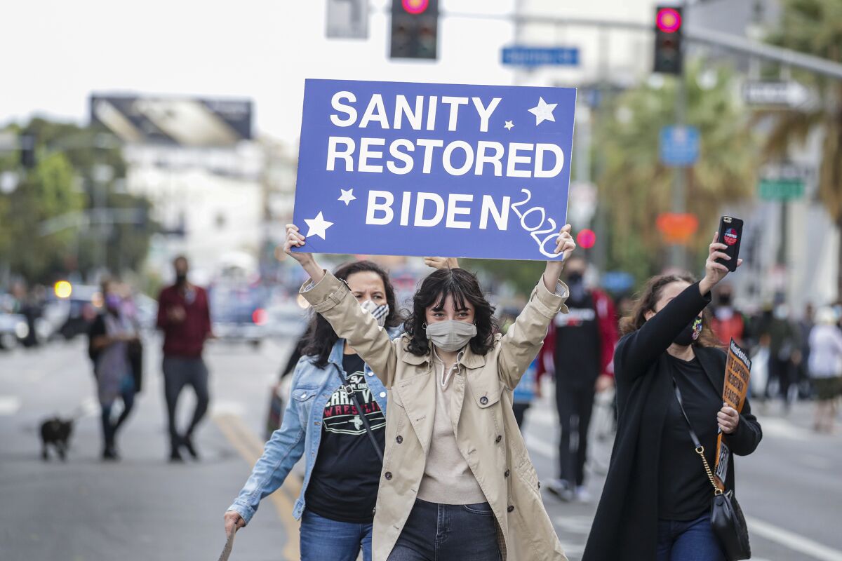 A woman holds up a sign that reads Sanity restored, Biden 2020