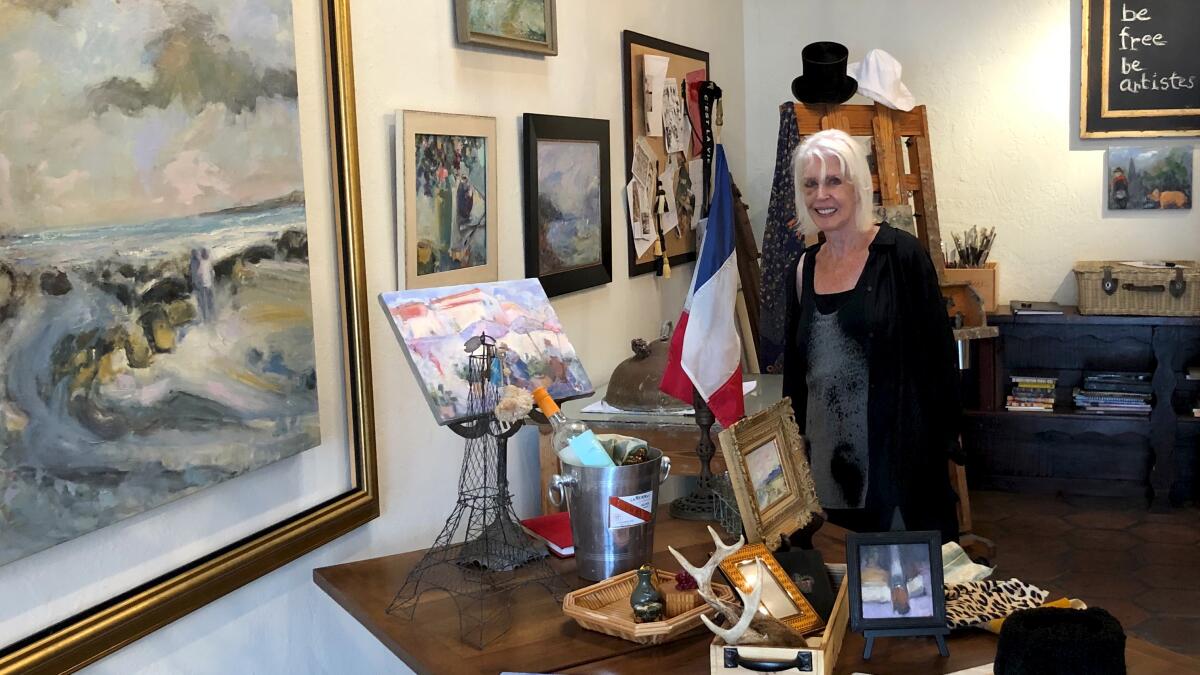 Contemporary impressionist painter Wendy Johnson stands in her Newport Beach gallery with her recent painting of Crystal Cove, left, which will be on display during the Art in the Park show Saturday.