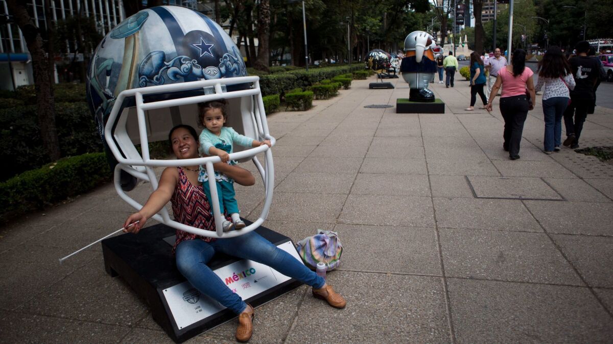 People pose for a picture inside a giant helmet, at an exhibition of footballs and helmets painted by Mexican artists, on Paseo de la Reforma in Mexico City.