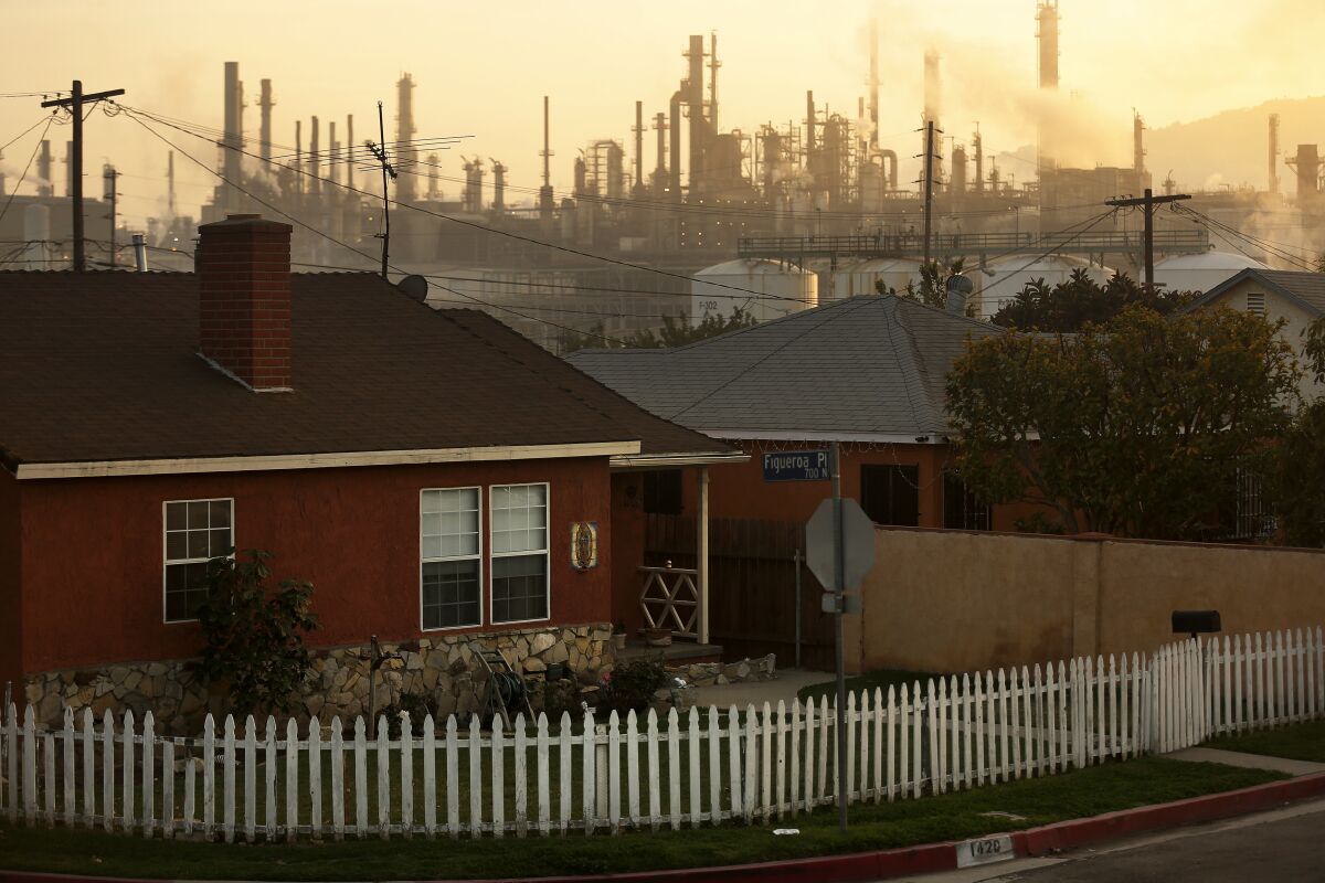A refinery serves as an backdrop for houses.