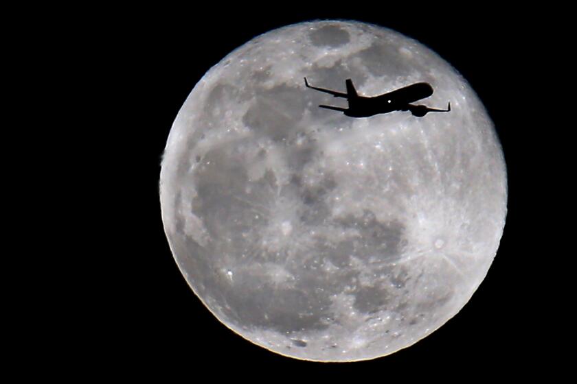A jetliner making an approach to LAX is silhouetted as it flies in front of the moon.