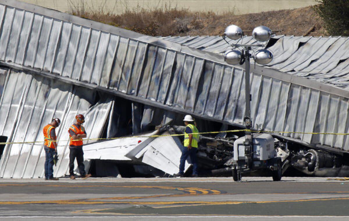 Investigators stand near the tail section of a twin engine Cessena jet plane outside an aircraft hangar at Santa Monica Airport on Sept. 30.