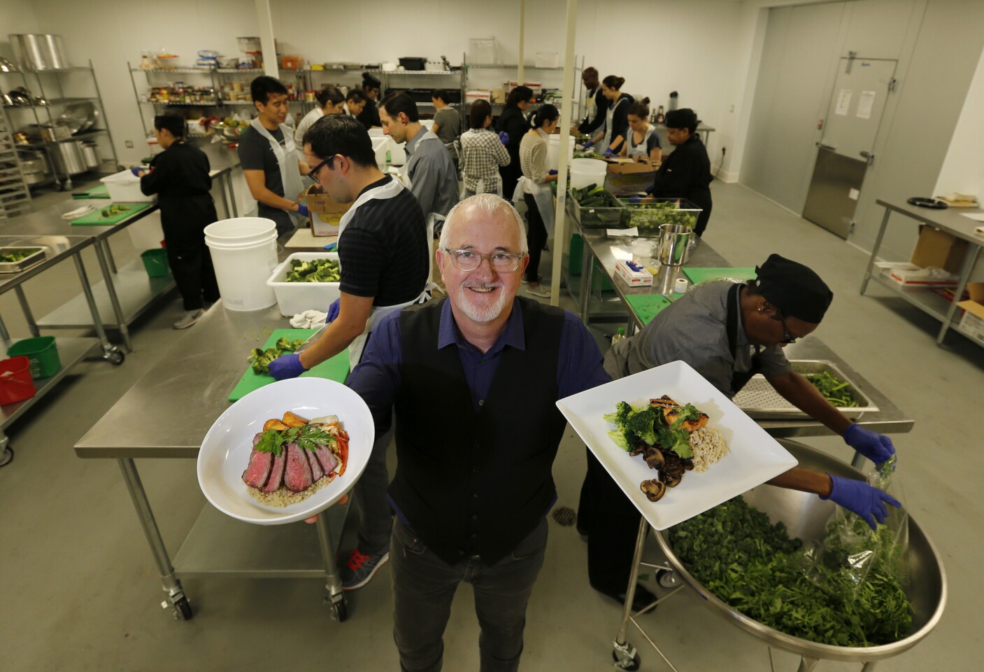 L.A. Kitchen founder Robert Egger holds meals made for the elderly by the workers, students and volunteers behind him. A major aim of the program is to provide job training to former inmates and young adults leaving the foster care system.