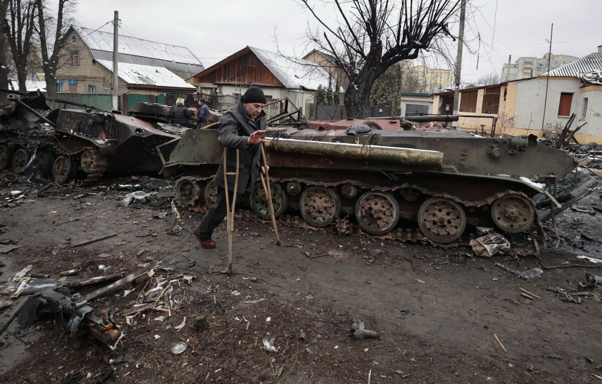 A man on crutches makes his way past destroyed military vehicles