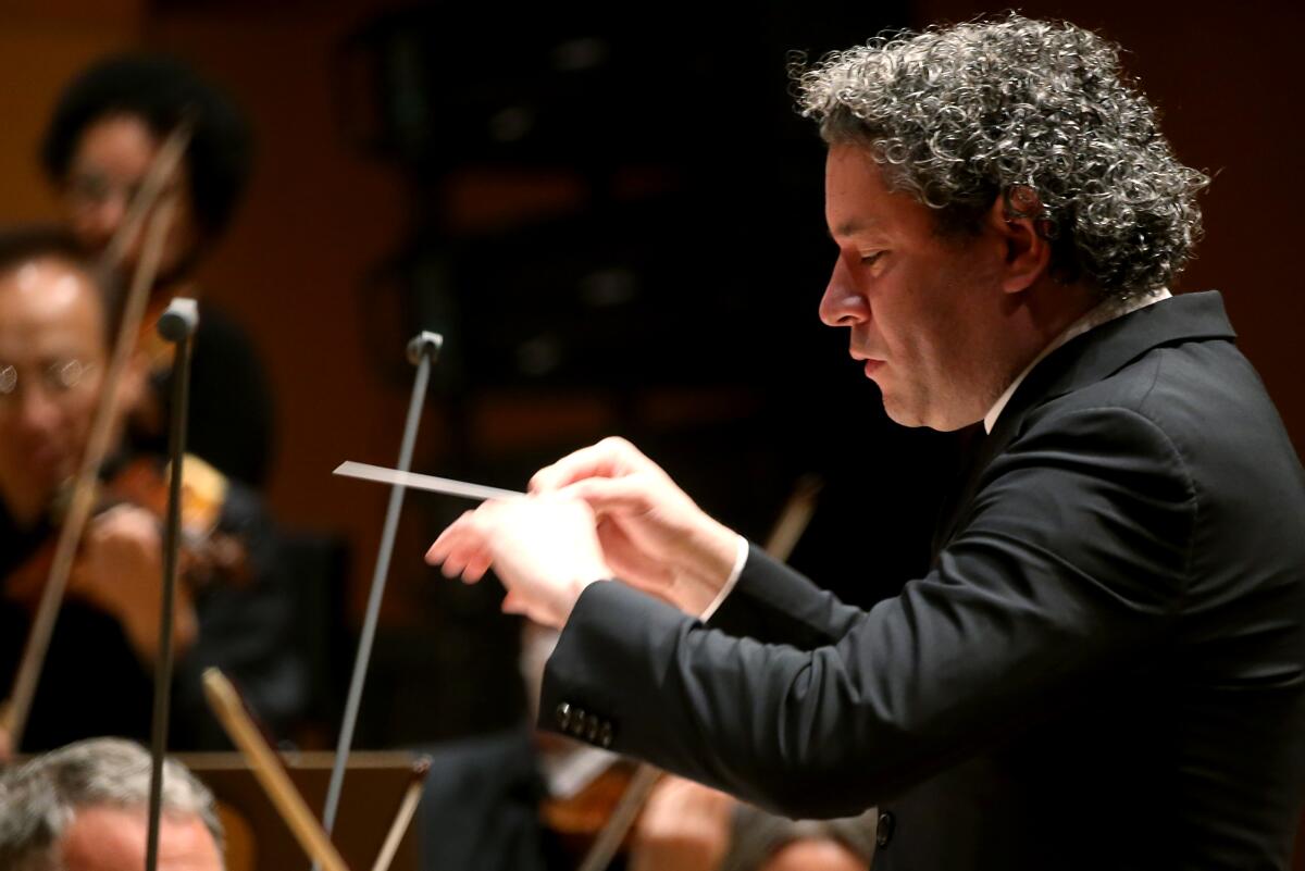 Gustavo Dudamel holds a baton. String players are seen beyond him.