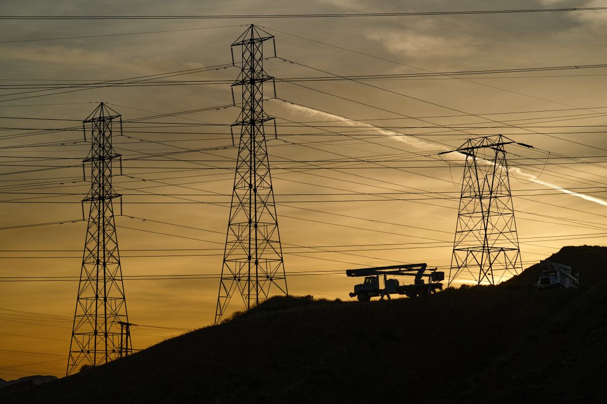 Silhouettes of cherry picker truck in front of electricity transmission towers.