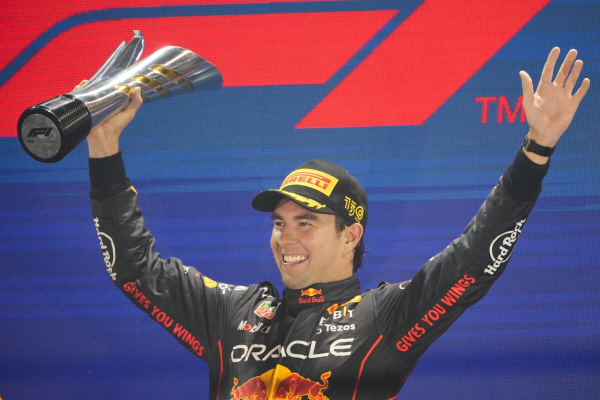 Sergio Perez holds up a trophy and his other arm and smiles.