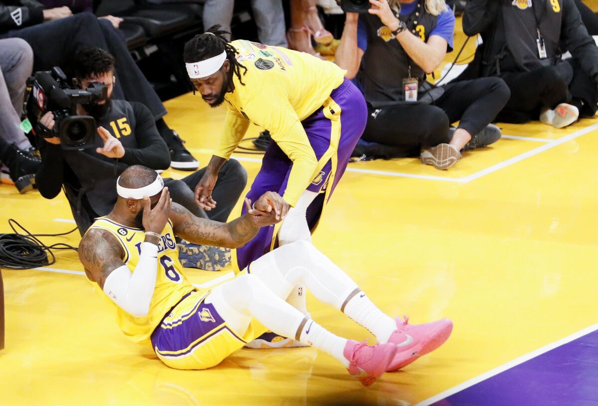 Lakers forward LeBron James is helped to his feet by teammate Patrick Beverley.