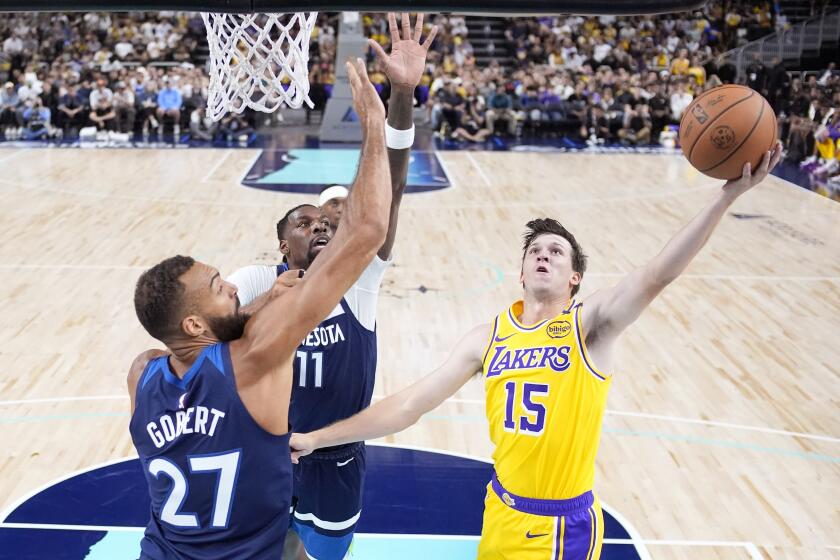 Los Angeles Lakers guard Austin Reaves, right, shoots as Minnesota Timberwolves center Rudy Gobert, left, and center Naz Reid defend during the first half of a preseason NBA basketball game, Friday, Oct. 4, 2024, in Palm Desert, Calif. (AP Photo/Mark J. Terrill)