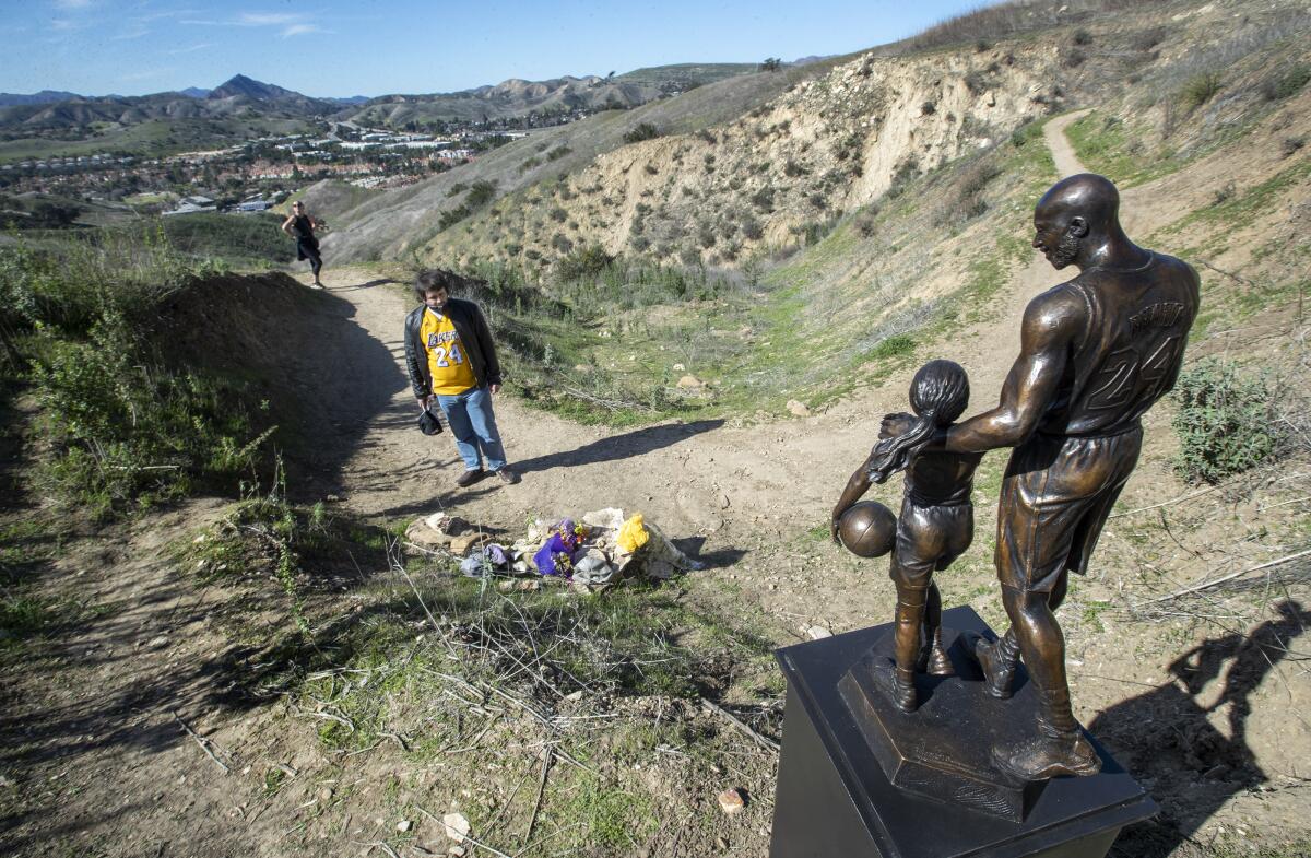 A man in a Lakers jersey stands before a bronze statue of a man and daughter who holds a basketball