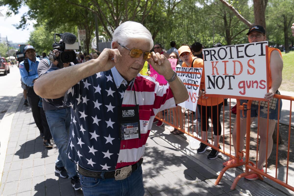 ARCHIVO - Un miembro de la Asociación Nacional del Rifle se tapa los oídos mientras camina junto a manifestantes