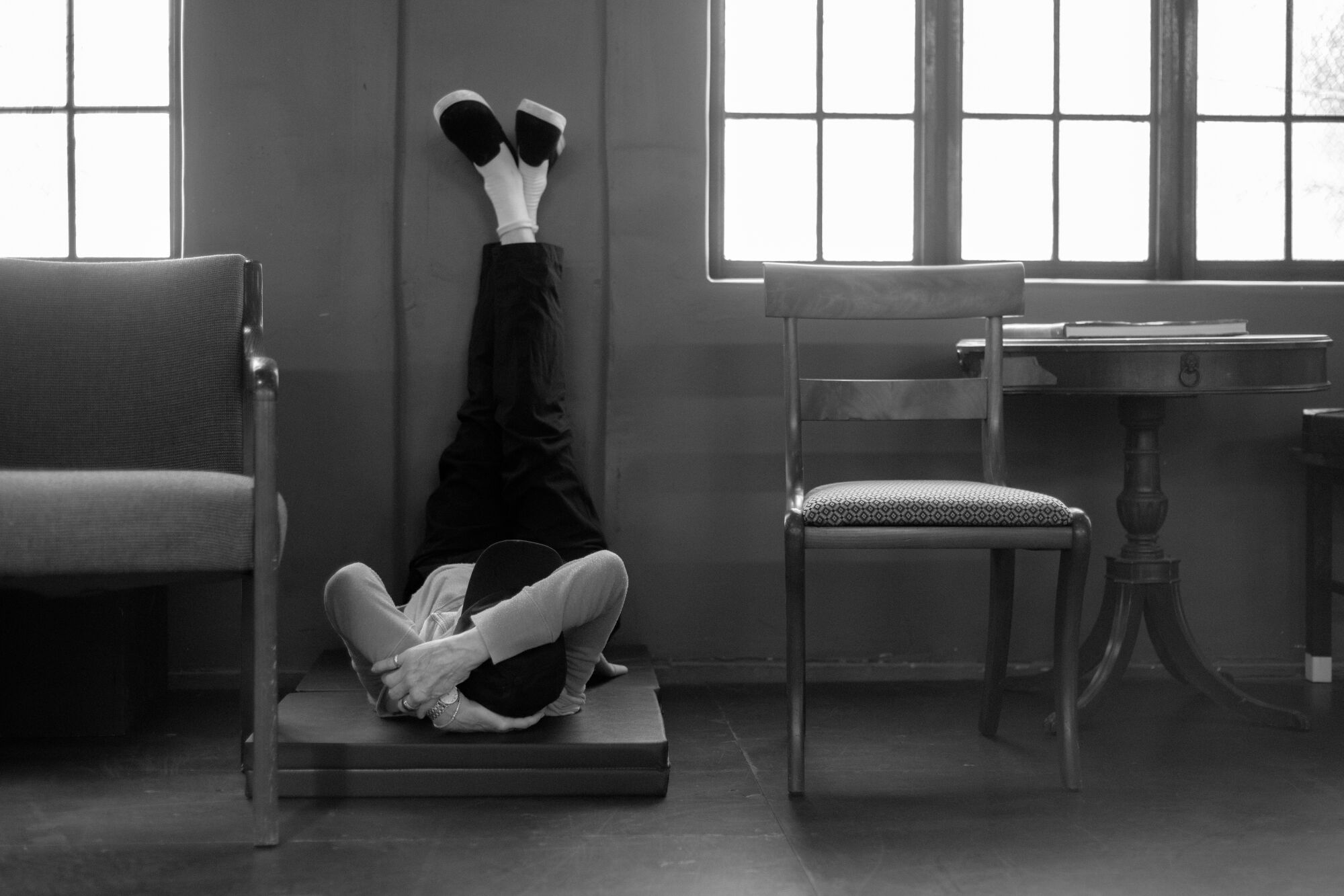 A woman lies on her back on the floor, her legs extended up against a wall. 