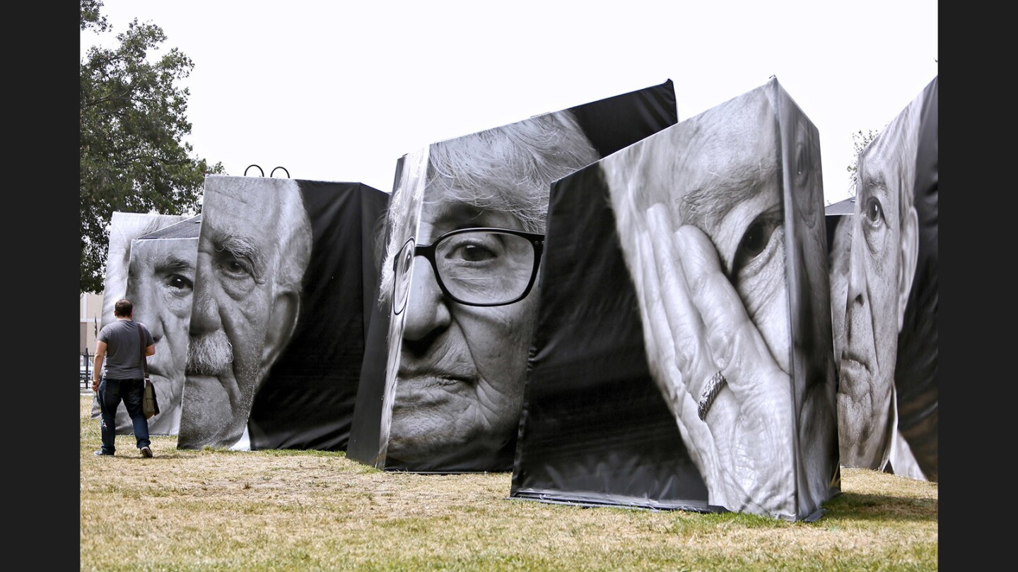 A man walks by an installation of Armenian Genocide survivors' portraits called iWitness, sponsored by the City of Glendale, Library Arts & Culture Dept., and the Community Services & Parks Dept., at Central Park in Glendale on Friday, May 5, 2017. The installation is of close-up portraits of the 1915 Armenian Genocide. According to the installation's description by Ramela Grigorian Abbamontian, PhD., "These portraits, like the survivors themselves, function as testimonies of the Genocide and the subsequent lives in the Diaspora." The explanation also states that "The survivors' direct, confrontational gazes are no longer those of terrified young children, but rather, they are the defiant eyes boldly looking out and claiming a place - a voice - in history." The design concept was by Narineh Mirzaeian and the iwitness draws its material from the archives of the Genocide Project.