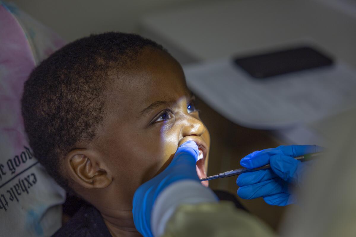 A 2-year-old boy opens his mouth for the dental hygienist as she checks his teeth.