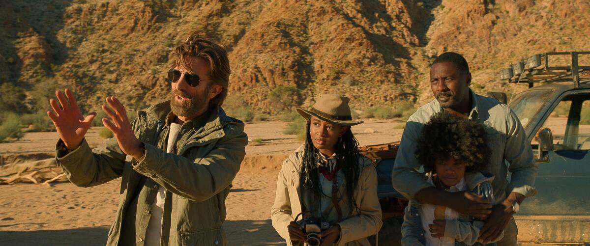 A man with sunglasses talks to a father and his two daughters outside a safari vehicle.