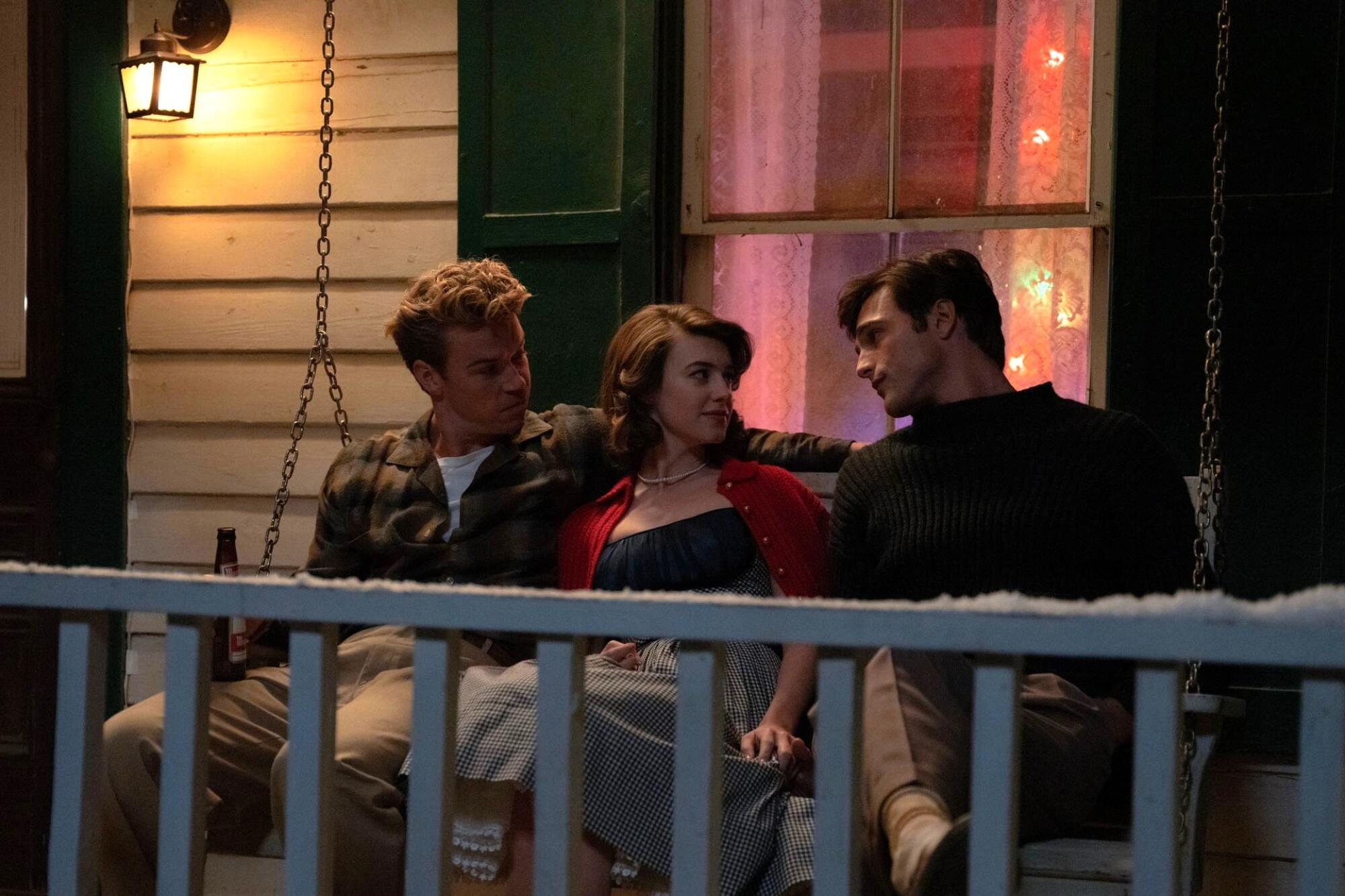 Three people sit on the porch swing of a suburban home.