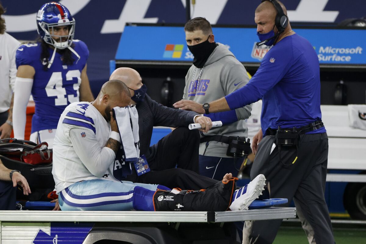 An emotional Dallas Cowboys quarterback Dak Prescott, wipes his face with a towel as he is carted off the field after suffering an unknown right lower leg injury in the second half of an NFL football game against the New York Giants in Arlington, Texas, Sunday, Oct. 11, 2020. The Giants' Nate Ebner (43) and staff look on. (AP Photo/Ron Jenkins)