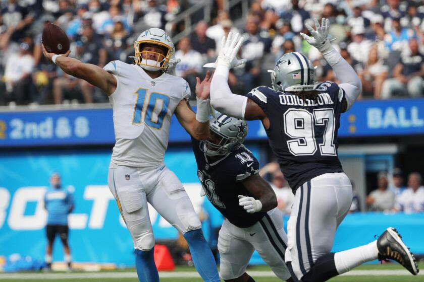 INGLEWOOD, CA - SEPTEMBER 19, 2021: Los Angeles Chargers quarterback Justin Herbert (10) gets his pass off as Dallas Cowboys linebacker Micah Parsons (11) and Dallas Cowboys defensive tackle Osa Odighizuwa (97) rush in for a sack at SoFi Stadium on September 19, 2021 in Inglewood, California.(Gina Ferazzi / Los Angeles Times)