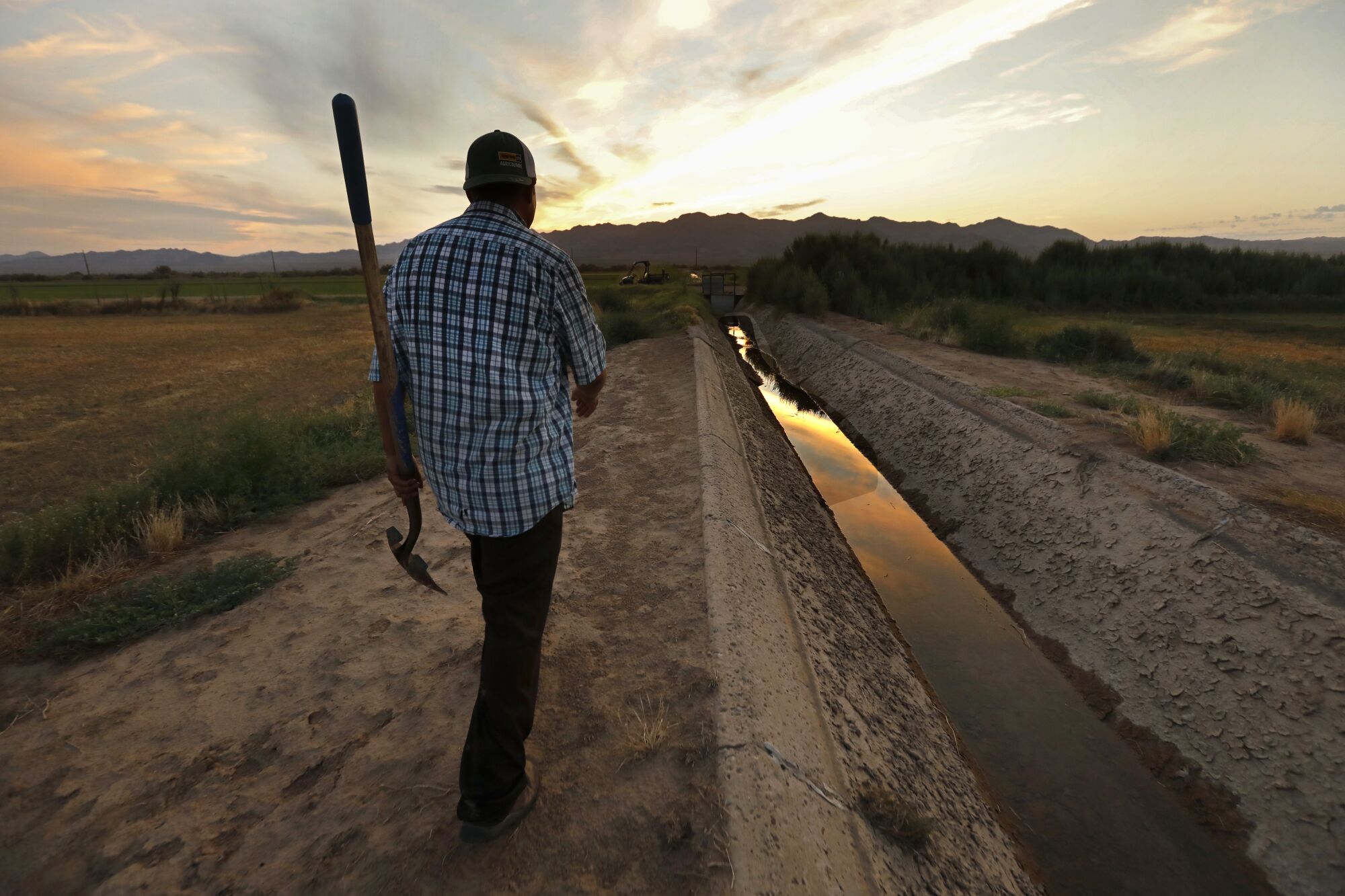 A man carrying a shovel walks between fields