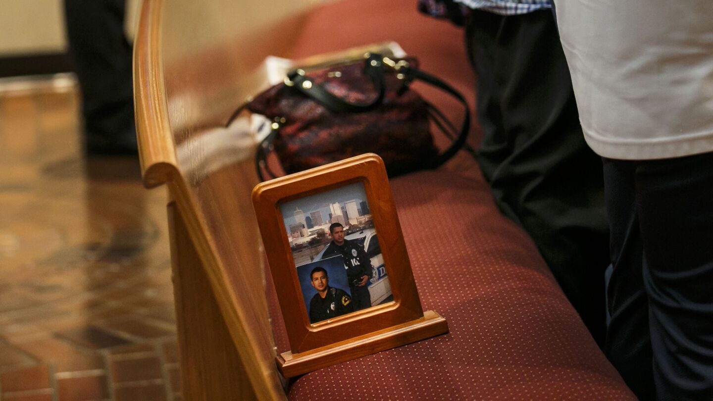 A picture frame with two portraits of slain police Officer Patrick Zamarripa sits on the pew as family members stand to pray during Sunday Mass at All Saints Catholic Church, in Dallas on July 10, 2016.