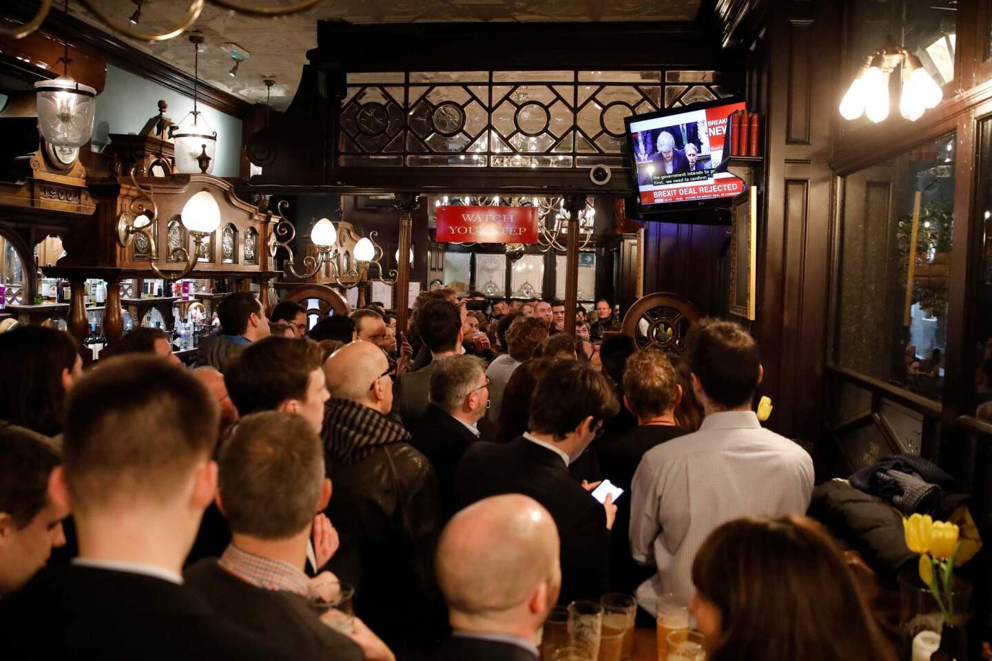 Patrons watch a television screen in the Red Lion public house on Whitehall, as it shows Britain's Prime Minister Theresa May speaking in the Houses of Parliament in London, after MPs vote against the government's Brexit deal.