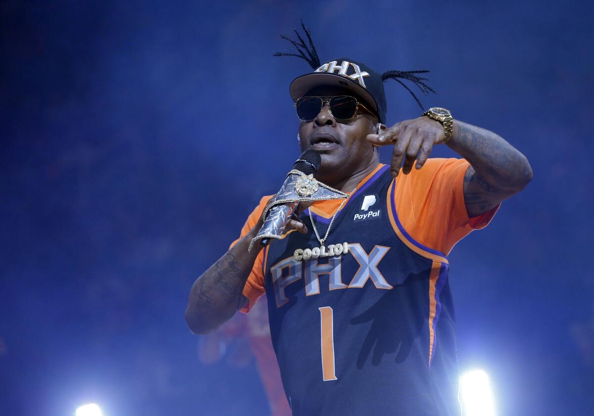 Coolio wears a cap and a Phoenix Suns basketball jersey while holding a microphone on stage