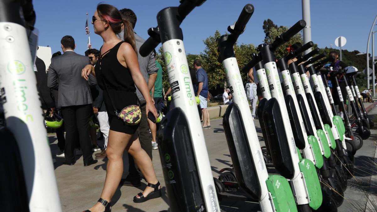 A woman walks past a row of parked Lime and Bird scooters during, "A Day Without a Scooter," rally in Santa Monica.