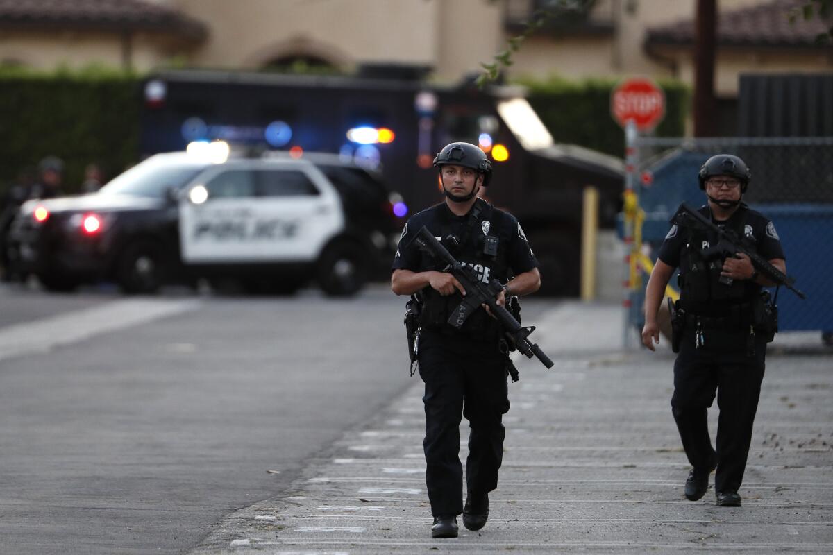 Police officers in helmets carry rifles while walking in a parking lot