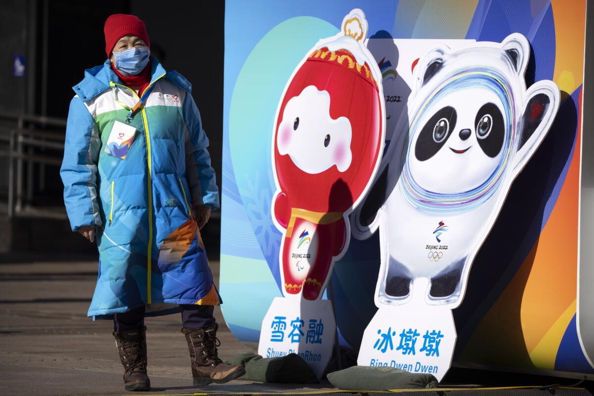 A woman in China poses next to figures of Winter Olympic mascots
