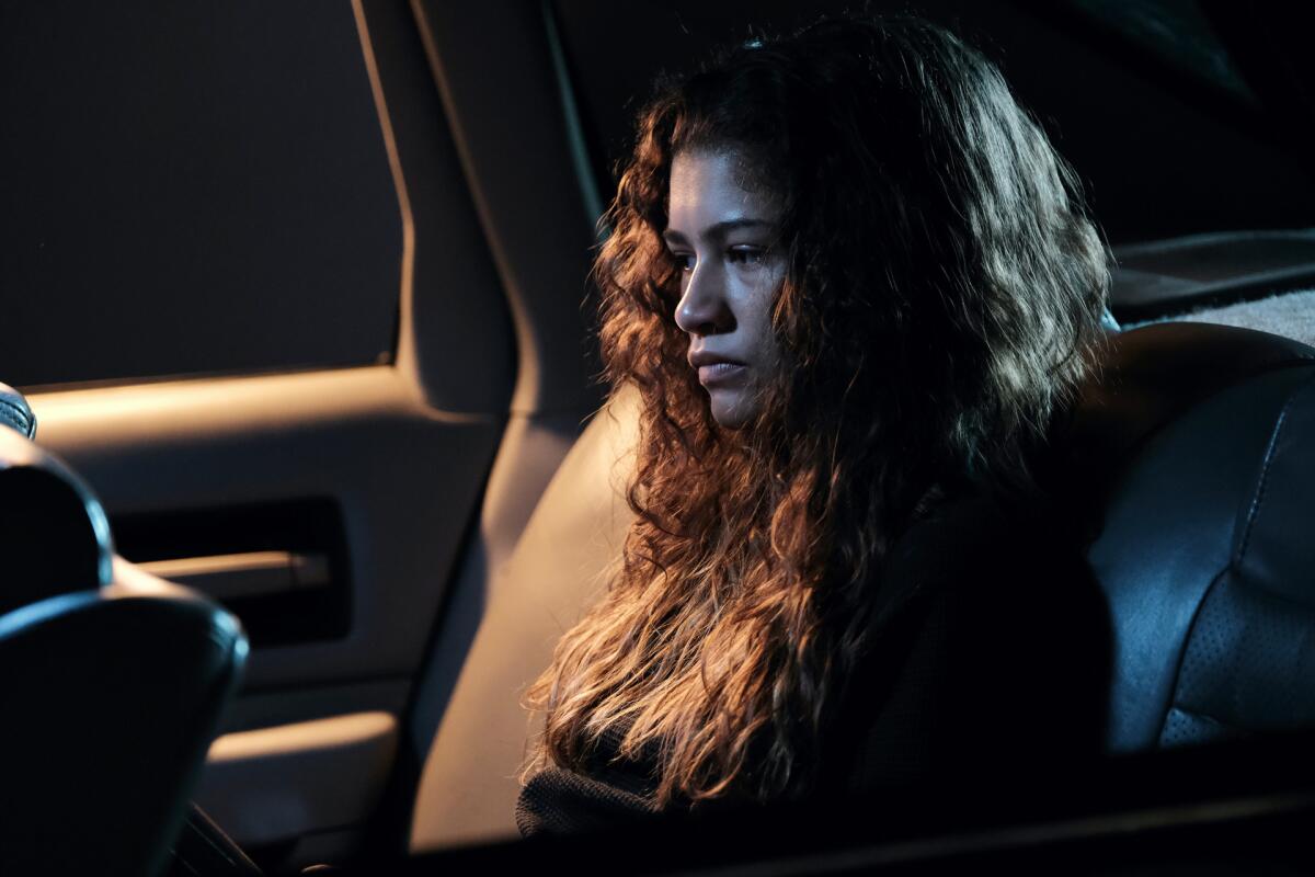 A young woman sits in a car at night.
