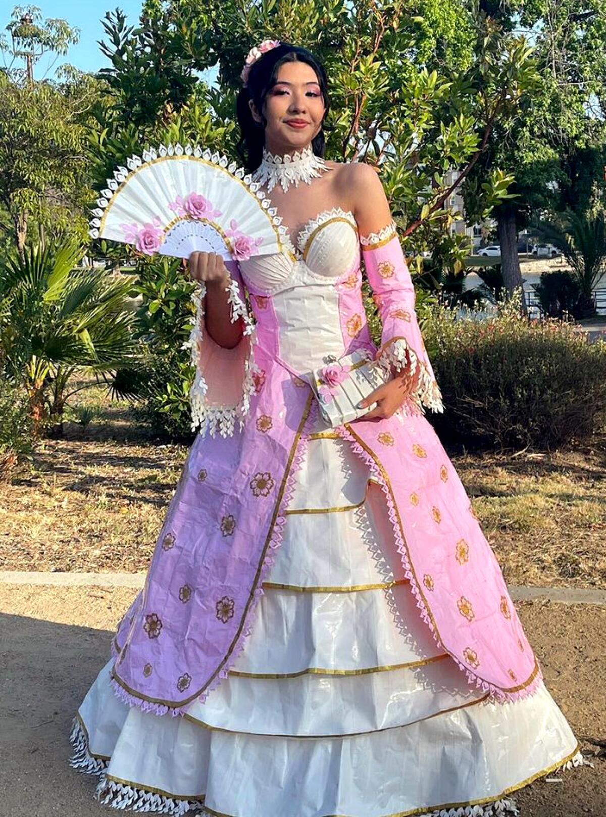 Karla Torres stands in her homemade pink and white duct tape prom dress. She holds a fan and wears a matching white choker.