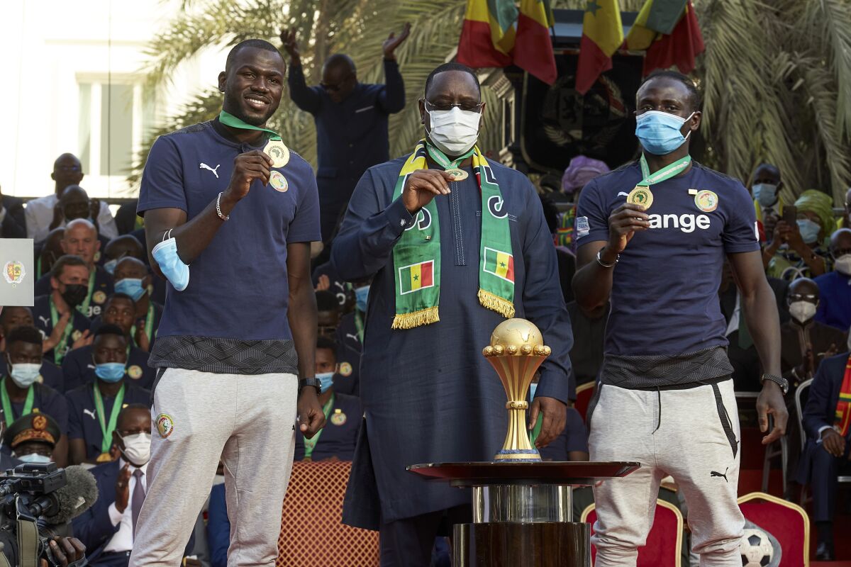 Senegal's President Macky Sall, center, stands with footballers Kalidou Koulibaly, left, and Sadio Mane, right, at a ceremony to mark the country's African Cup win, at the presidential palace in Dakar, Senegal Tuesday, Feb. 8, 2022. Senegal won its first African Cup Sunday by beating Egypt 4-2 in a penalty shootout with Sadio Mane scoring the decisive penalty. (AP Photo/Stefan Kleinowitz)